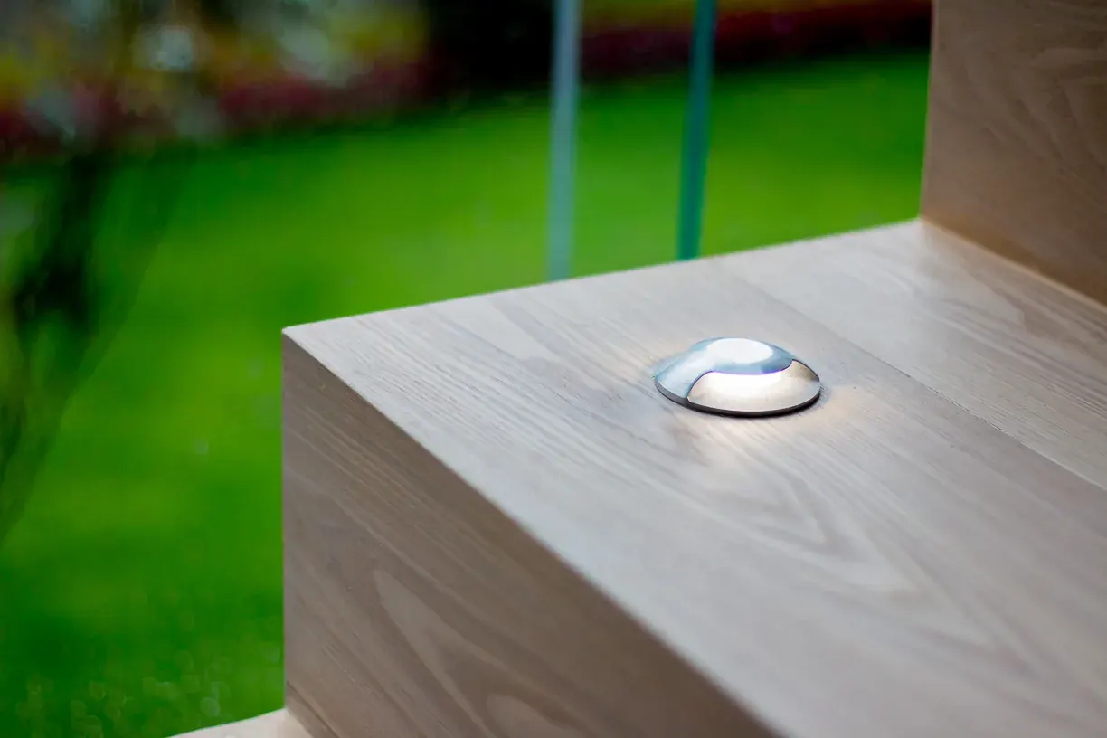 Detalle de una luminaria empotrada en el canto de piedra, contra el verde del jardín