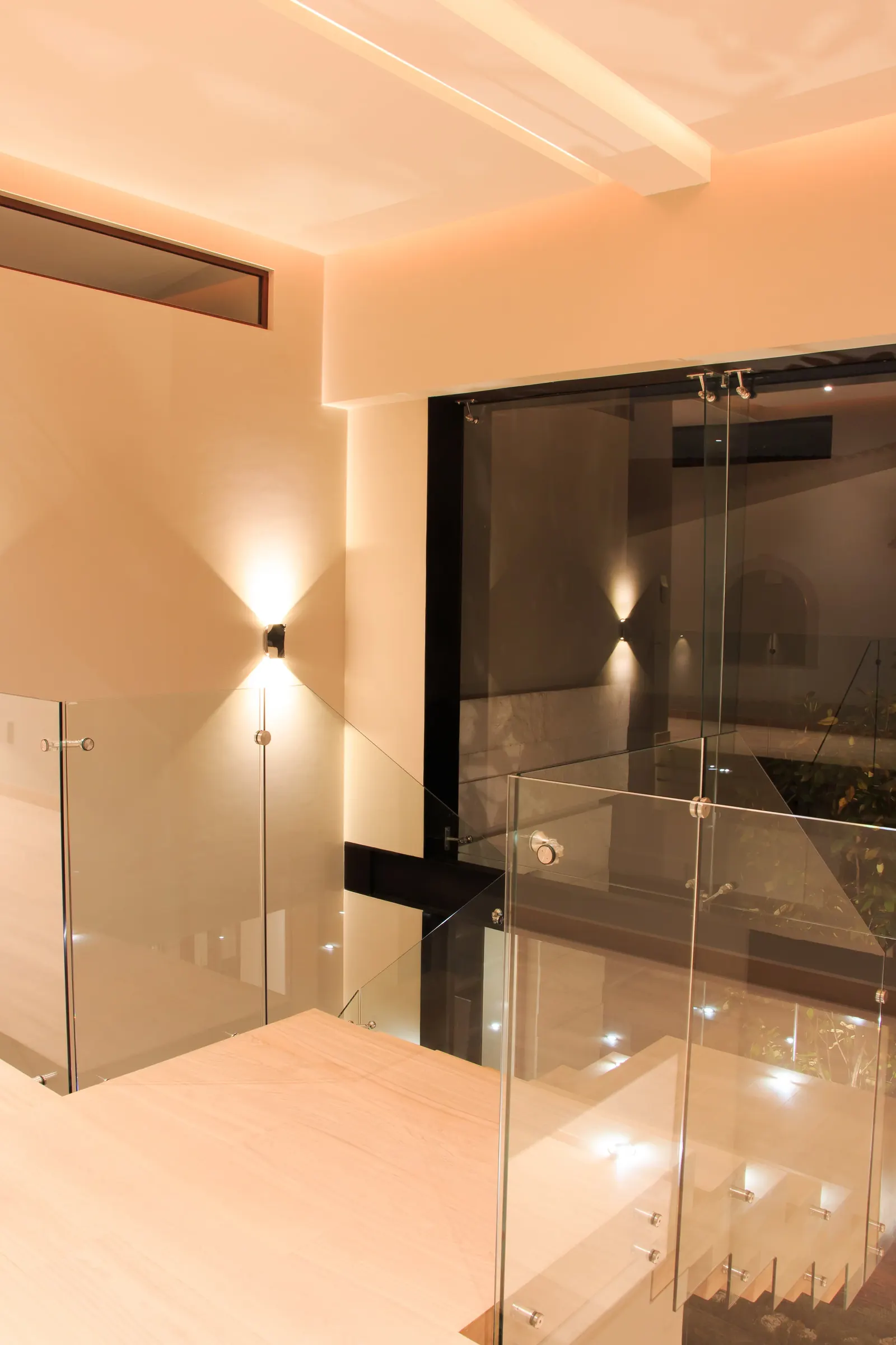 Descanso de la escalera, con el barandal de cristal y una luminaria de muro