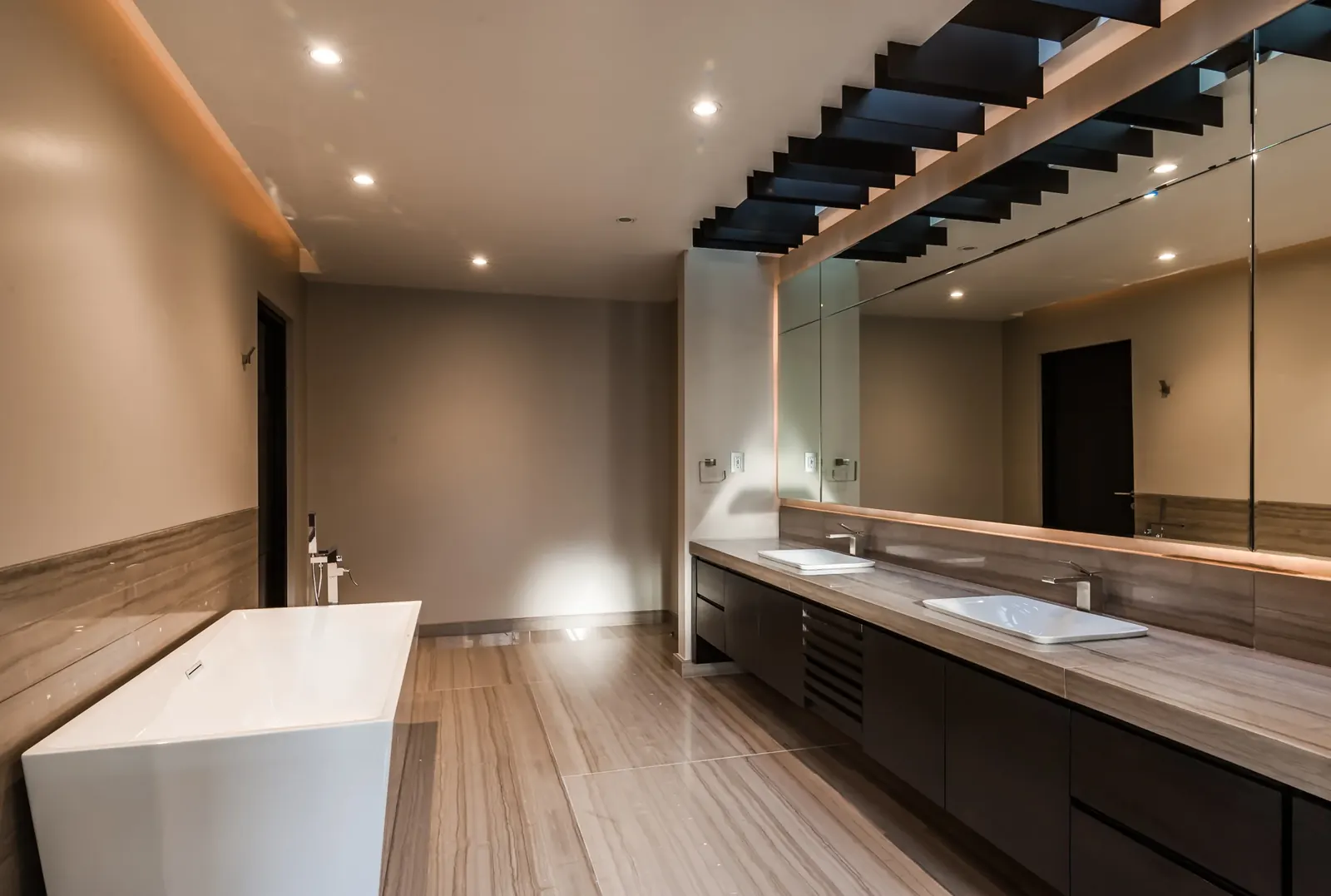 Baño con tina exenta bajo la escalera, y doble lavabo frente al espejo
