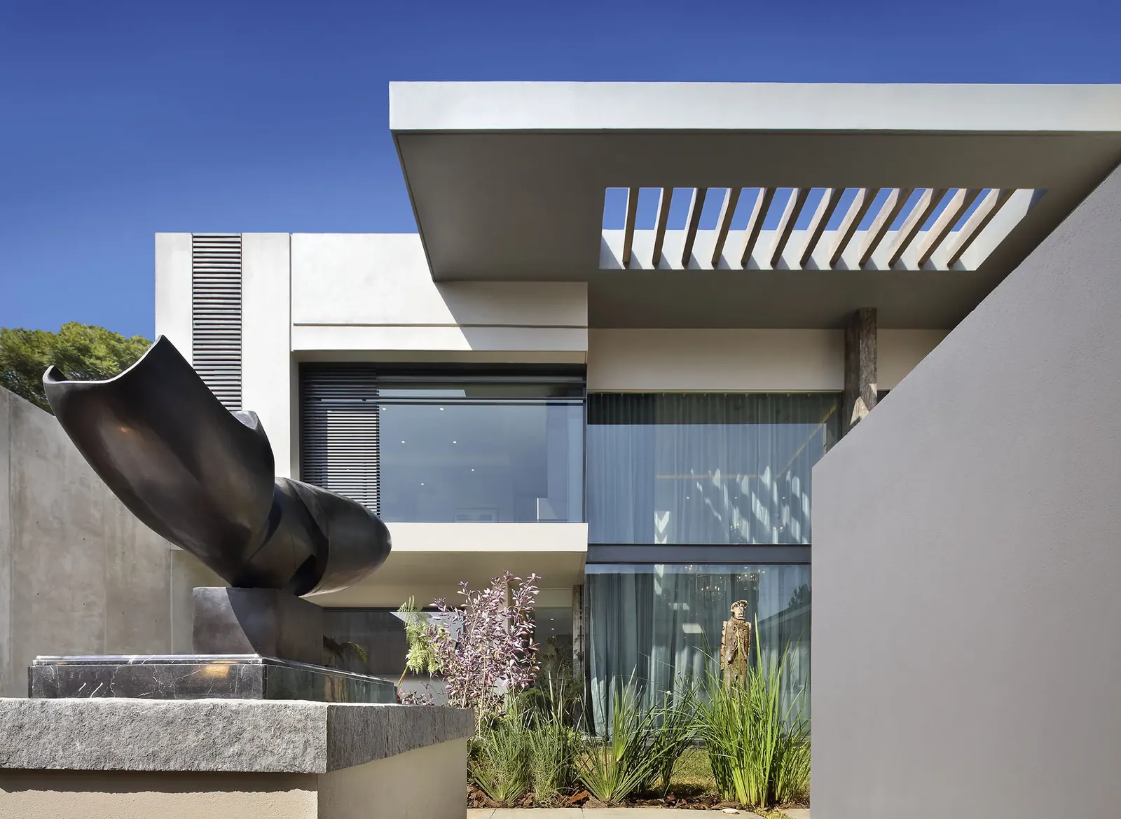Fachada con una escultura oscura sobre el espejo de agua del acceso