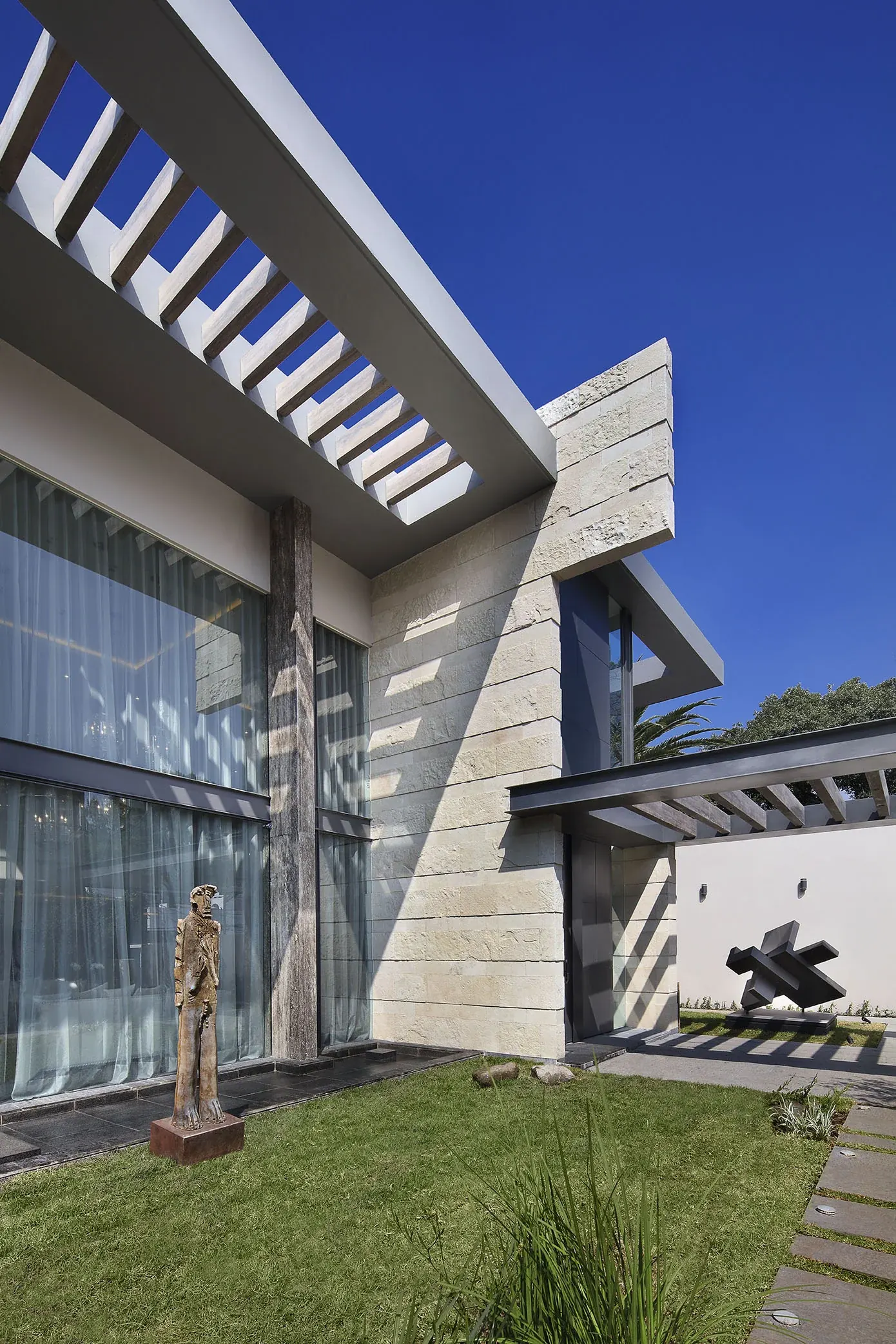 La casa desde el jardín, con el volumen de piedra y la pérgola de concreto