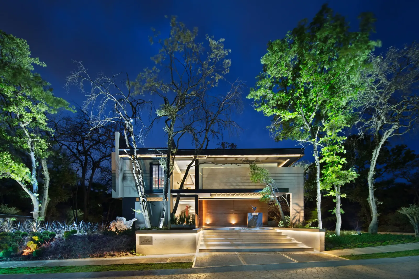 Fachada al anochecer, con los árboles del terreno iluminados desde el piso