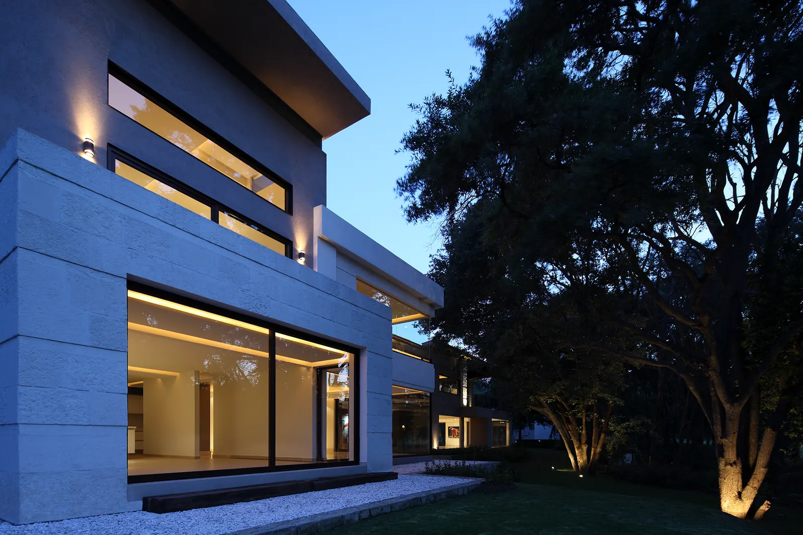 Fachada lateral al anochecer, con la ventana horizontal iluminada