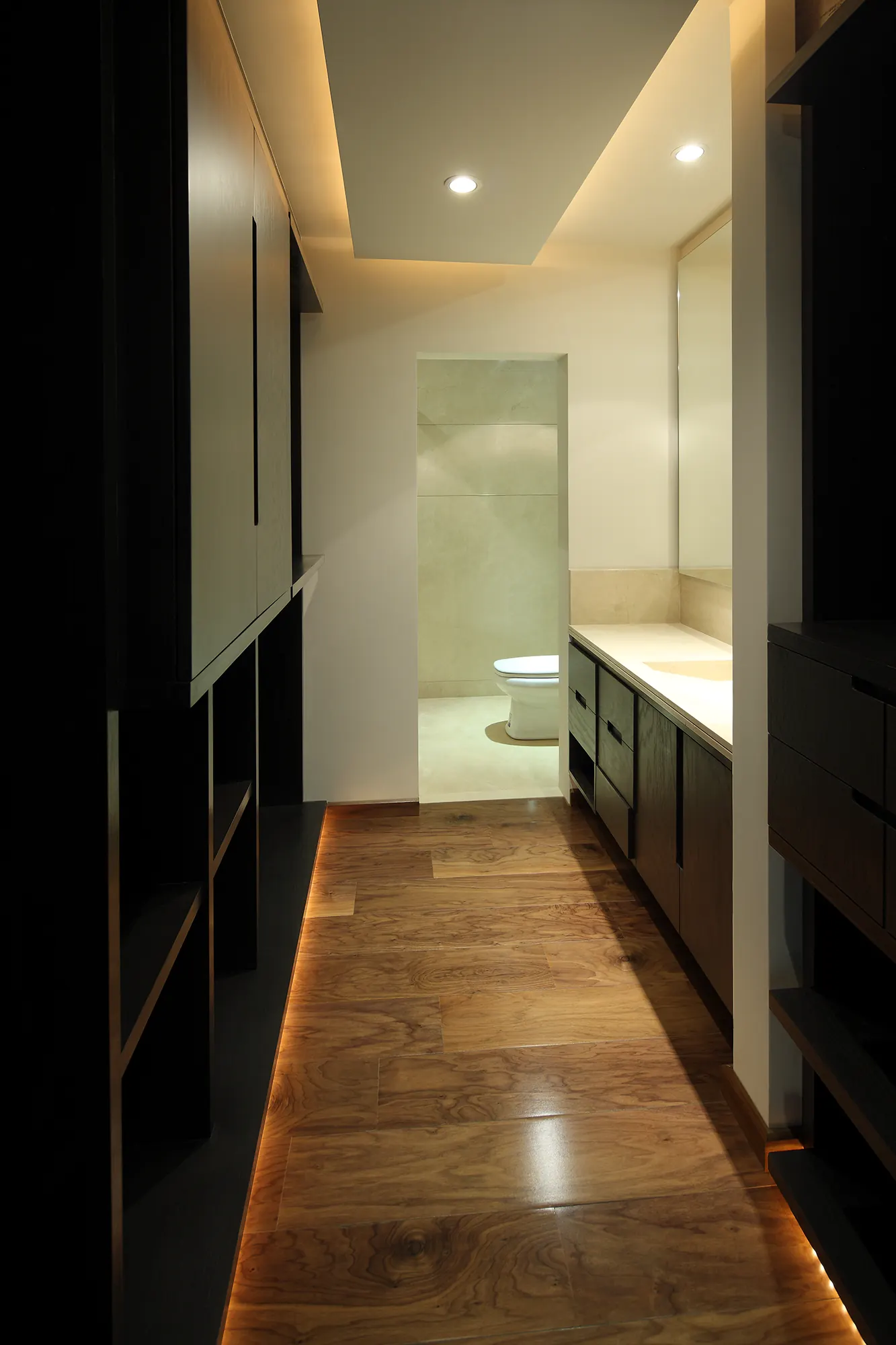 Pasillo hacia el baño, con piso de madera y luz rasante